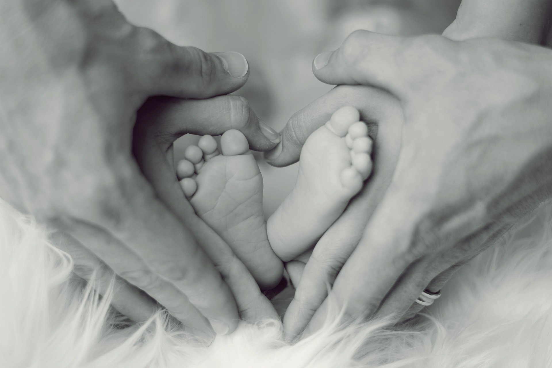 Händer der Mutter und des Vaters über den Füßen des Babys in Herzform
